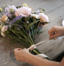 Händer som binder ett band runt en bukett med blommor på ett träbord.